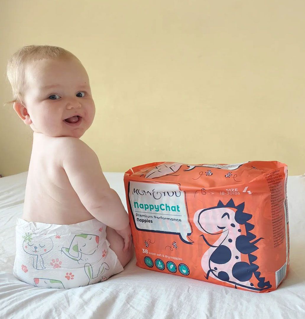 A cozy baby sits on a bed in Mum & You Eco Nappies—super soft, breathable, and dry for 12 hours, with fun Nappychat characters for bonding!