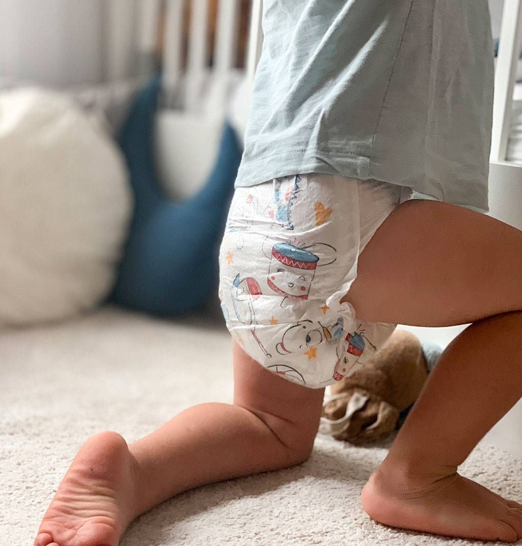 A toddler in Mum & You nappies stands on the floor, highlighting a playful and innocent moment of early childhood.