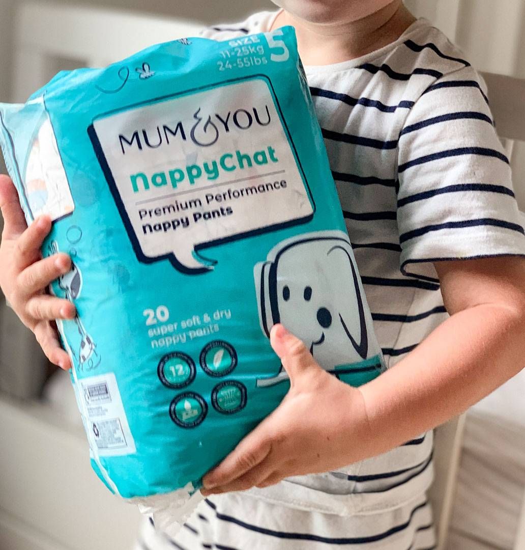 A young boy smiles while holding a package of Mum & You nappy pants, capturing a moment of care and responsibility.