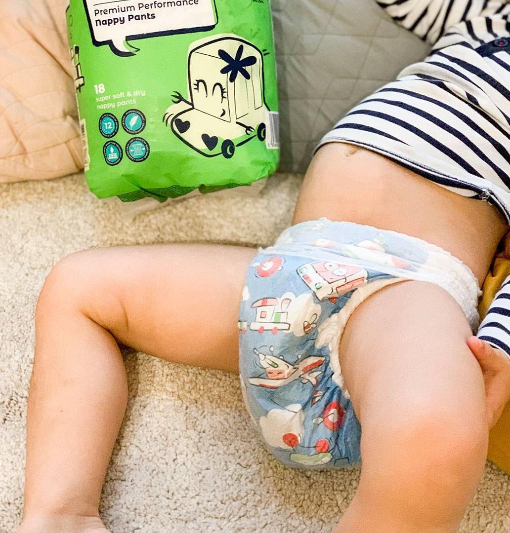 A baby in Mum & You nappies happily holds a bag of nappies, capturing a playful moment of early childhood.